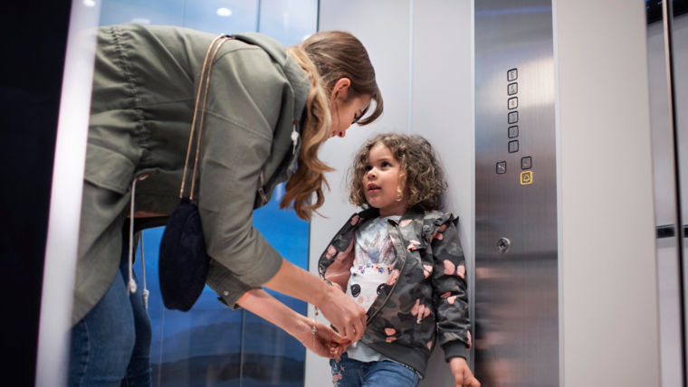 Mother adjusting child's jacket inside an elevator - KONE